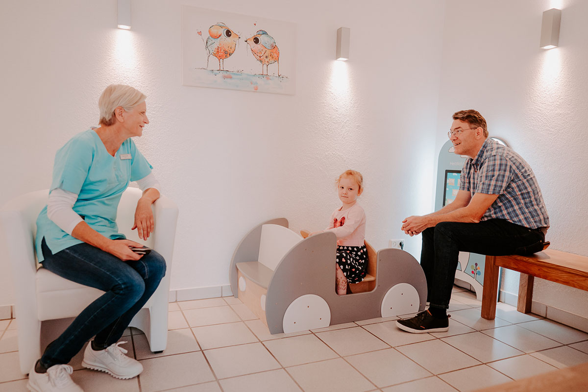 Eine Mitarbeiterin im Gespräch mit dem Vater einer kleinen Patientin bei ihrem ersten Besuch beim Kinderzahnarzt in Einbeck