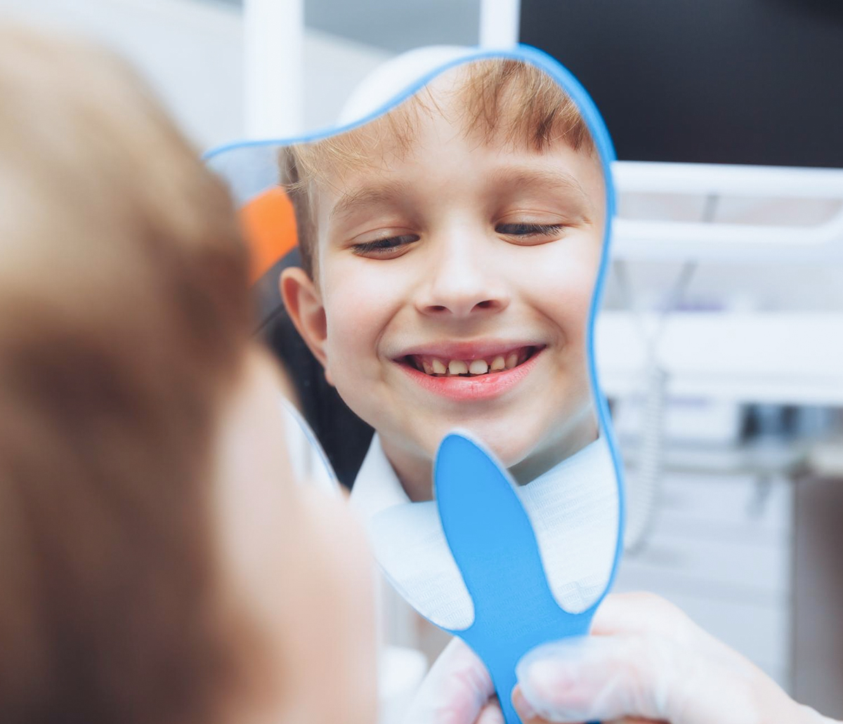 Kind betrachtet sein Lächeln nach einer kinderzahnärztlichen Behandlung im Spiegel