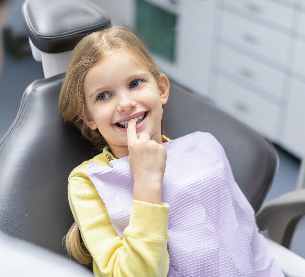 Kind zeigt auf einen Milchzahn während eines entspannten Zahnarztbesuchs